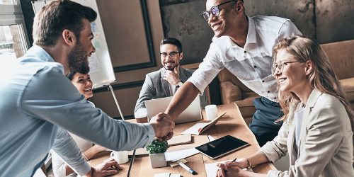 Welcome to our team! Top view of young modern men in smart casual wear shaking hands while working in the creative office